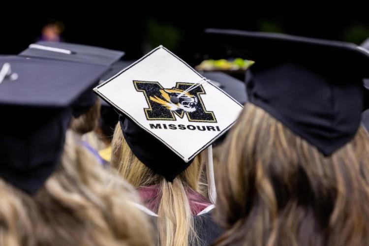 Close-up of graduates in black caps and gowns; one white cap displays the University of Missouri tiger logo, capturing a celebratory commencement mood.