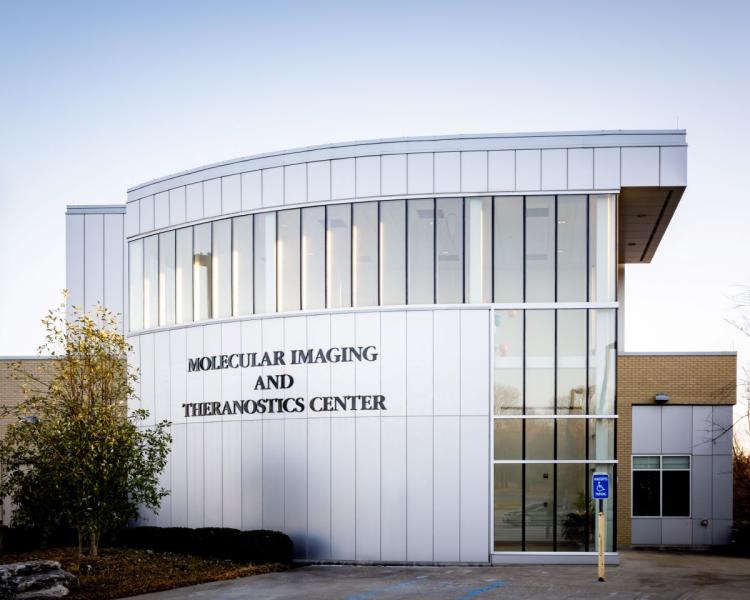Curved modern building labeled "Molecular Imaging and Theranostics Center." Features large windows, sleek design, and an accessible parking sign.